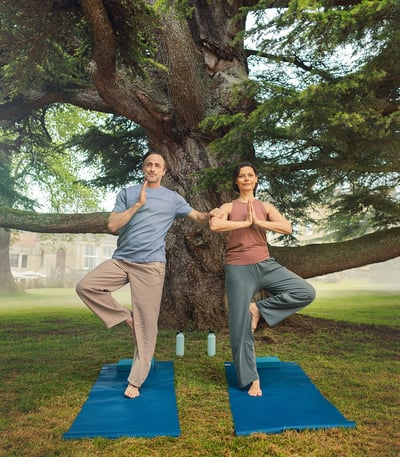 A couple doing yoga, the man using the woman as a support, on the grounds at Heythrop Park