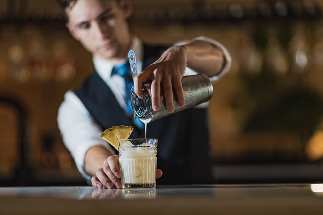 A stylish barman in a suit serves a drink into a glass at the bar of the Runnymede on Thames hotel.